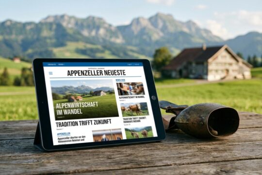 Tablet auf Holztisch zeigt die neuesten Nachrichten Appenzellerland, daneben eine Kuhglocke. Dahinter die grüne Landschaft mit Bauernhaus und Alpen.