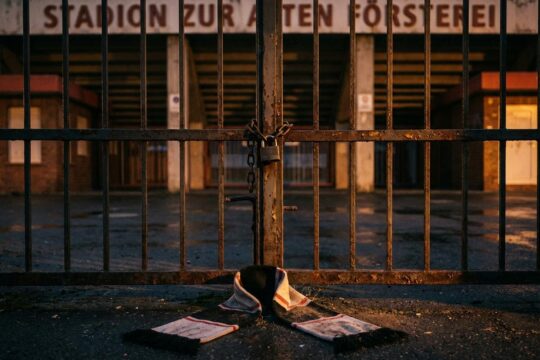 Verschlossenes Eisentor eines menschenleeren Fußballstadions bei Dämmerung mit zerfetztem Fanschal, Sinnbild für die Borussia Neunkirchen Insolvenz.