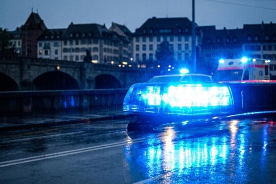 Blaue Blitzlichter von Einsatzfahrzeugen spiegeln sich nachts auf regennasser Basler Strasse. Ein Sinnbild für die Dringlichkeit der Blaulicht Einsätze Basel.