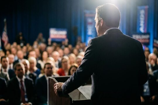 Ein energischer, männlicher Redner, von hinten am Pult stehend, gestikuliert vor Delegierten. Er repräsentiert den neuen AfD Spitzenkandidat MV bei einer wichtigen Ankündigung.