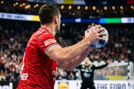 Muskulöser kroatischer Handballer im roten Trikot mit Ball, bereit für den entscheidenden Wurf im spannungsgeladenen Kroatien Handball EM Halbfinale.