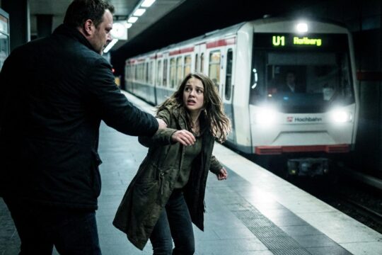 Ein kräftiger Mann zerrt eine panische Frau gewaltsam über einen U-Bahnsteig. Die U-Bahn Hamburg rast heran, sie blickt verzweifelt.