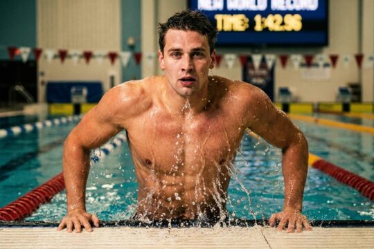 Ein muskulöser Schwimmer taucht dynamisch nach seinem kraftvollen Zielschlag aus dem Wasser, triumphierend über den Rex Maurer 1000 Freistil Rekord.