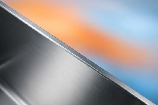 Präzise Kante eines gebürsteten Edelstahlpaneels spiegelt hohe Qualität wider, dahinter symbolisiert ein farblicher Wärme-Kälte-Verlauf die Effizienz der Edelstahl Vakuumisolierung.