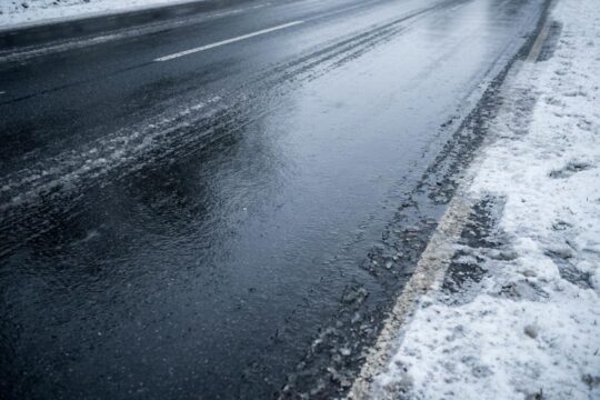 Eine tückisch spiegelglatte Asphaltstraße am frühen Wintermorgen in Norddeutschland. Die winterliche Glättegefahr Norddeutschland ist deutlich sichtbar.