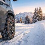 Robuste Schneeketten für Wohnmobil professionell montiert an einem Reifen auf einer verschneiten Bergstraße bei Sonnenuntergang. Berge im Hintergrund.