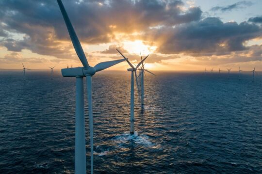 Majestätische Offshore-Windkraftanlagen in goldener Abendsonne auf dem Meer. Sie repräsentieren den komplexen Ausbau Offshore-Windkraft.