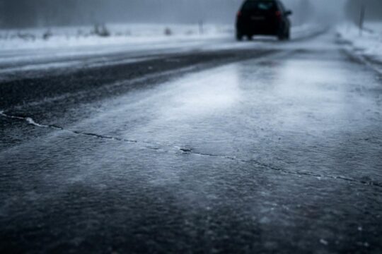 Eine dunkle, spiegelglatte Asphaltstraße mit tückischem Blitzeis spiegelt kaltes Licht und warnt vor Glatteis in Niedersachsen.