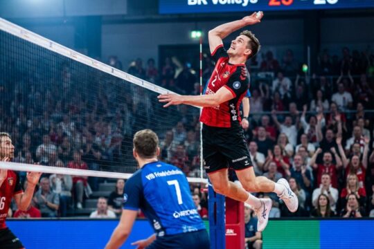 Ein BR Volleys Spieler schmettert entschlossen den Volleyball am Netz, ein VfB Friedrichshafen Spieler wehrt ab. Intensiver Moment im Topspiel BR Volleys VfB Friedrichshafen.