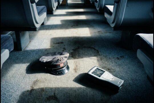 Auf dem Zugboden liegen eine zerknitterte Schaffnermütze und ein Scanner. Die Szene mit langen Schatten verdeutlicht die bedrückenden Folgen von Gewalt gegen Zugpersonal.