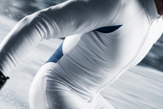 Aerodynamischer weißer Rennanzug im Fokus. Seine Farbe und glatte Textur visualisieren Geschwindigkeit im verschwommenen Pistenhintergrund.