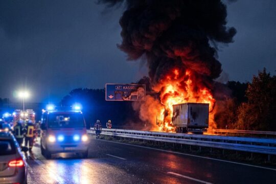 Nächtlicher Lkw-Brand A7 bei Kassel: Ein Sattelzug brennt lichterloh. Hohe Flammen und Rauch steigen auf. Blaulichter auf nasser Autobahnfahrbahn.