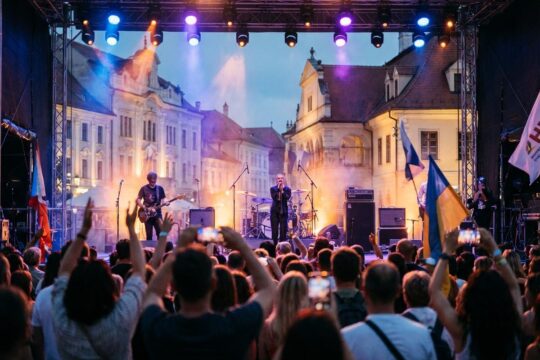 Energiegeladene Dämmerungsszene mit begeistertem Publikum vor farbig beleuchteter Open-Air-Bühne, die das Kulturarena Jena 2026 Programm zelebriert.