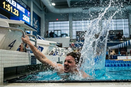 Ein Schwimmer beendet dynamisch sein Rennen, Hand trifft Ziellinie mit Wasserschwall. Dies zeigt die Spannung der Cavalier Invite 2026 Ergebnisse.