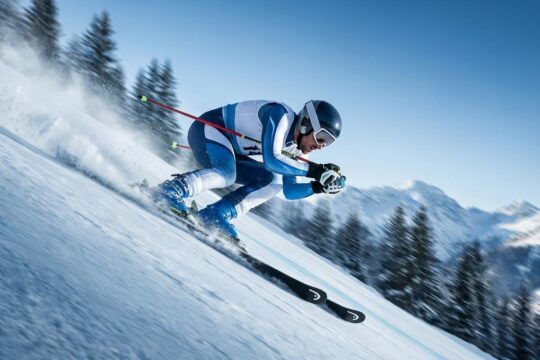 Ein Skirennfahrer rast dynamisch die extrem steile, eisige Olympia Abfahrt Stelvio in Bormio hinab. Schnee spritzt unter den Skiern.