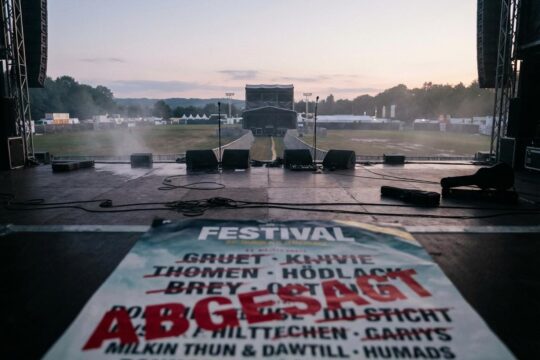 Eine menschenleere Festivalbühne bei Dämmerung mit einem zerknitterten Plakat, auf dem "ABGESAGT" steht. Die Stimmung spiegelt die Enttäuschung über die Kid Rock Festival Absagen wider.