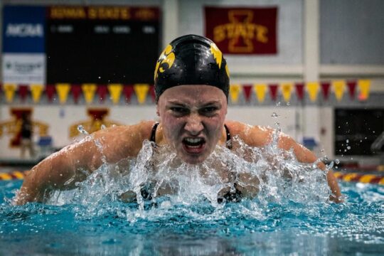 Eine Schwimmerin des Iowa Schwimmteams durchbricht kraftvoll die Wasseroberfläche, ihr energischer Blick zeigt den Sieg über Iowa State.