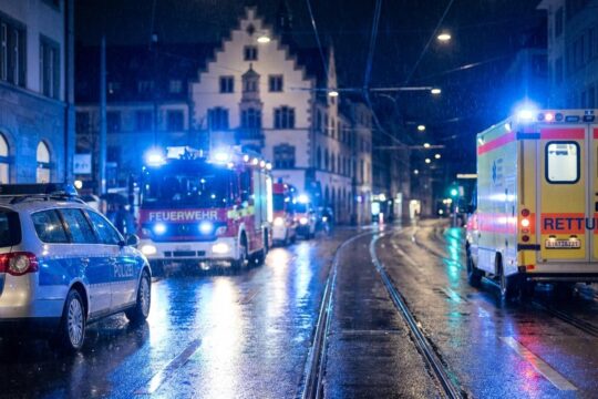 Intensive blaue Sirenenlichter von Einsatzfahrzeugen wie Polizei und Feuerwehr spiegeln sich nachts auf nassen Strassen der Blaulicht Region Basel wider.