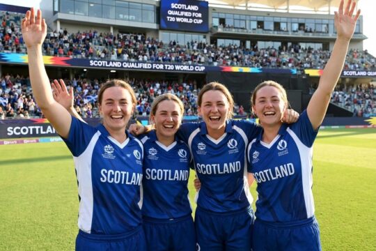 Jubelnde schottische Cricket-Spielerinnen in blau-weißen Trikots auf dem Spielfeld feiern ihren Sieg bei der Schottland Frauen T20 WM Qualifikation vor jubelnden Fans.