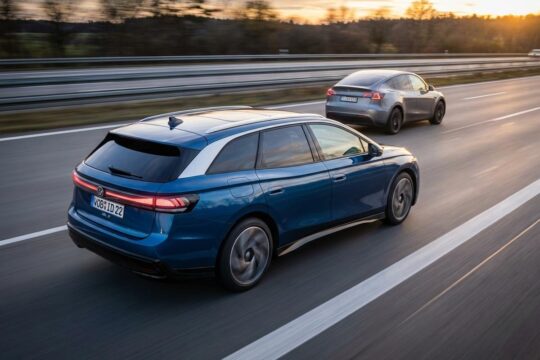 Ein moderner, elektrischer VW ID.7 überholt dynamisch ein Tesla Model Y auf einer europäischen Autobahn bei Sonnenuntergang. Hier überholt VW Tesla bei Elektroautos.