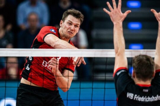 BR Volleys Spieler im Sprung führt einen kraftvollen Angriffsschlag gegen den VfB Friedrichshafen aus, der Ball kurz vor den Händen, Gegner versucht Block.