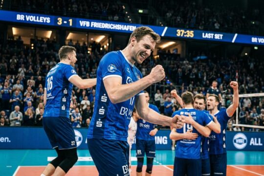 BR Volleys Spieler in blauen Trikots feiern ekstatisch den BR Volleys Sieg gegen Friedrichshafen. Ein Athlet springt hoch, das Team jubelt vereint.