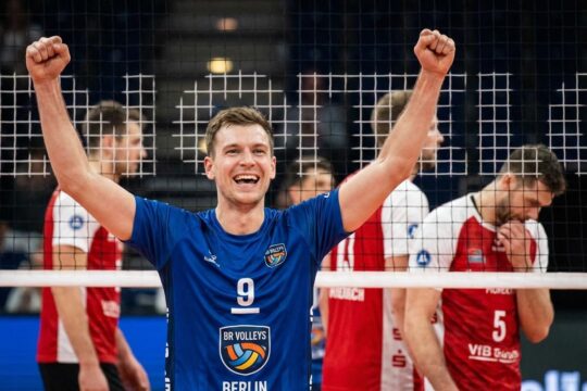 Ein BR Volleys Spieler jubelt nach dem hart erkämpften BR Volleys Sieg gegen Friedrichshafen, sein Gesicht strahlt Freude, die Arme sind erhoben. Hinten enttäuschte Gegner.