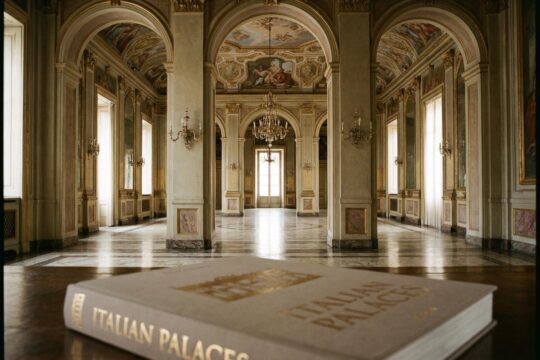 Opulente Enfilade eines italienischen Barockpalastes mit Fresken, Goldstuck und Marmorböden. Ein Bildband italienische Paläste liegt davor.