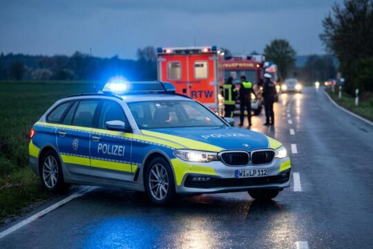Polizeieinsätze am Wochenende in Hessen: Polizeiwagen mit Blaulicht leuchtet nachts auf feuchter Straße, weitere Einsatzfahrzeuge im Hintergrund.