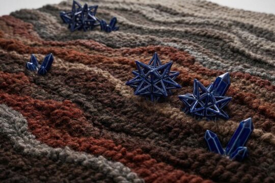 Nahaufnahme des Porzellanteppichs Leuchtenburg: Erdige Wolltexturen in Braun, Rot, Grau mit filigranen, schimmernden tiefblauen Porzellankristallen, die an Mineralien erinnern.