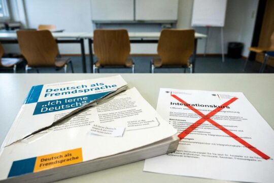 Ein aufgeschlagenes Sprachlehrbuch mit zerschnittener Seite und Integrationskurs-Flyer mit X verdeutlichen Kürzung der Integrationskurse.