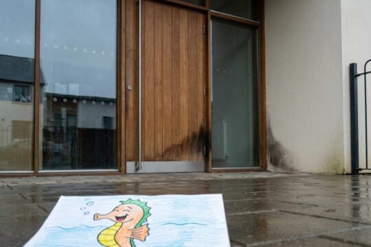 Verschlossener Haupteingang der Kita Seepferdchen Bous mit einem Feuchtigkeitsfleck, der auf Schimmel hinweist. Ein Kinderbild liegt davor.