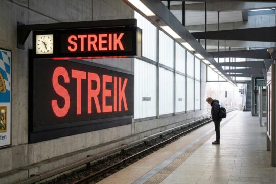 Leerer U-Bahnsteig in Bayern morgens, eine Anzeige meldet 'STREIK'. Ein Pendler blickt frustriert auf die Gleise – Folge des Nahverkehr Streik Bayern.