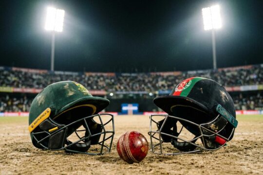 Beschädigte Cricket-Helme von Südafrika und Afghanistan liegen auf staubigem Pitch. Ein roter Ball und Flutlicht beleuchten die Dramatik der T20 WM.