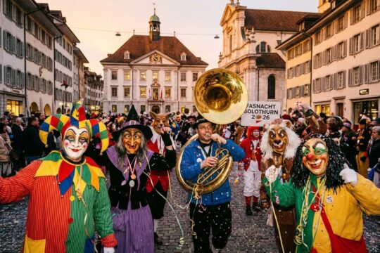 Bunte Fasnächtler mit Masken spielen Guggenmusik, Konfetti fliegt durch Solothurns Gassen. Fasnacht Solothurn 2026.