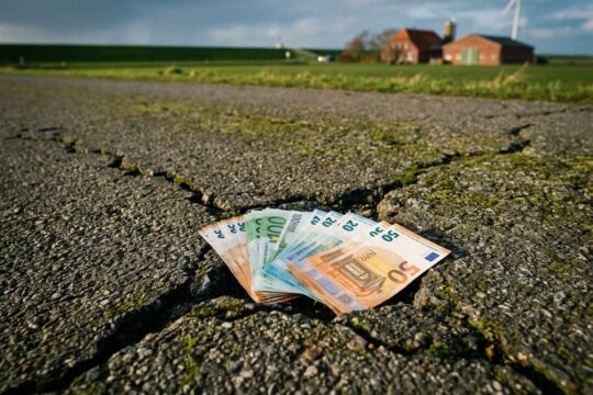 Frische Euro-Banknoten stecken in einem tiefen Riss einer alten Straße, was die begrenzte Wirksamkeit des Sondervermögens Schleswig-Holstein andeutet.