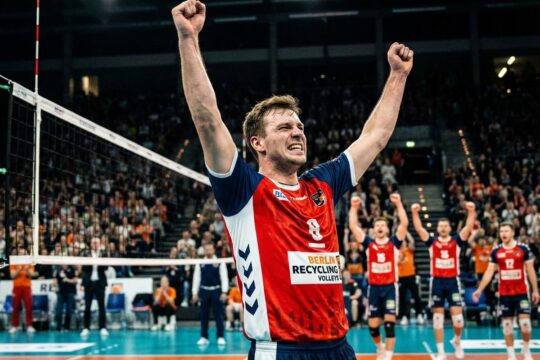 BR Volleys Sieg Friedrichshafen: Ein Spieler im rot-weiß-blauen Trikot springt jubelnd, die Arme hochgestreckt, Freude und Erleichterung im Gesicht.