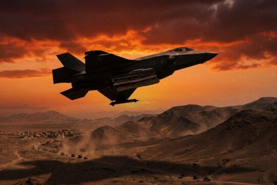Moderner US-Kampfjet in bedrohlicher Silhouette über staubiger Wüste unter rotem Abendhimmel. Ein Bild des drohenden US Militäreinsatz Iran.