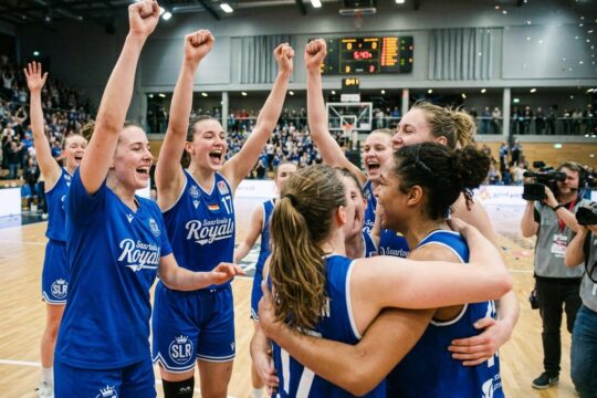 Die Saarlouis Royals feiern euphorisch ihren Sieg über Hannover. Mehrere Spielerinnen jubeln mit erhobenen Armen im königsblauen Trikot auf dem Feld.