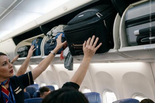Southwest Airlines Gepäckfächer Streit: Passagiere stopfen Gepäck in übervolle Fächer, Flugbegleiterin resigniert wegen Platzmangel.
