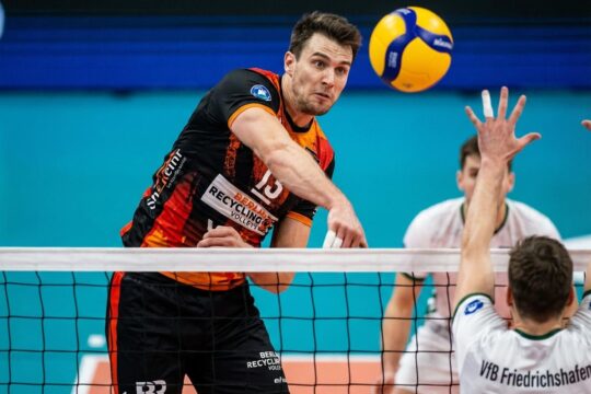 BR Volleys Spieler schlägt den Ball im entscheidenden Moment über das Netz, während ein Spieler des VfB Friedrichshafen den Block nicht schafft. Intensive Szene des Spitzenspiels.