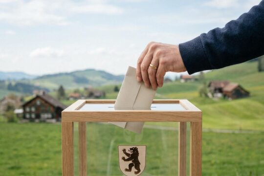 Eine Wählerhand wirft einen Stimmzettel in eine Wahlurne mit Appenzeller Wappen. Symbol für die Nationalratswahl Appenzell Ausserrhoden, im Hintergrund sanfte Hügel.