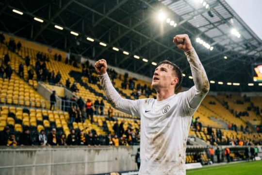 Ein SV Elversberg Spieler jubelt emotional nach dem 2:1-Sieg im Rudolf-Harbig-Stadion über Dynamo Dresden, mit enttäuschten Fans im Hintergrund.