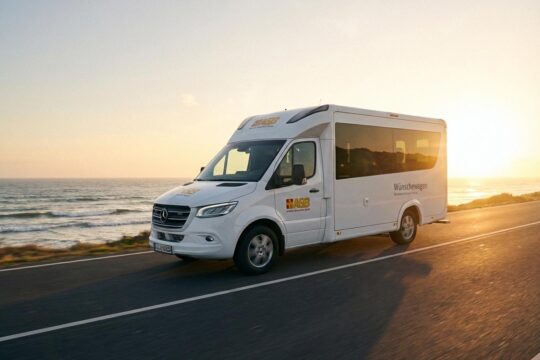 Ein moderner, weißer ASB Wünschewagen fährt auf einer malerischen Küstenstraße in den goldenen Sonnenuntergang, um letzte Wünsche wahr werden zu lassen.