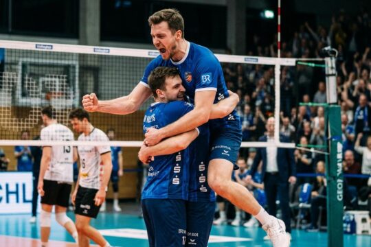 BR Volleys Spieler in blauen Trikots feiern begeistert ihren BR Volleys Sieg Friedrichshafen. Einer springt, ein Teampartner umarmt ihn vor frustrierten Gegnern.