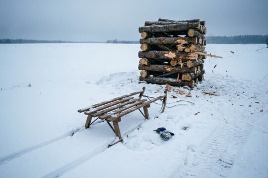 Ein zerbrochener Holzschlitten und ein Kinderhandschuh liegen im Schnee bei einem Baumstammstapel mit Einschlagsspuren, Zeugen des tödlichen Schlittenunfalls Kuchelmiß.