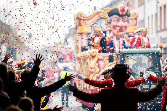 Dynamisches Bild eines Rosenmontagsumzugs im Saarland mit einem Meer aus wirbelndem Konfetti über jubelnden Menschen vor bunten Motivwagen.