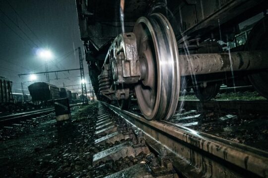 Nahaufnahme eines Güterwagenrads auf glänzenden Schienen im Dämmerlicht des Rangierbahnhofs. Die verschwommene Bewegung visualisiert den störenden Lärm Rangierbahnhof Muttenz.