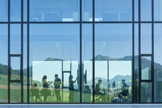 Moderne Glasfassade in Freiburg spiegelt Voralpen und Menschen bei der Arbeit, repräsentativ für den Arbeitsmarkt Kanton Freiburg.