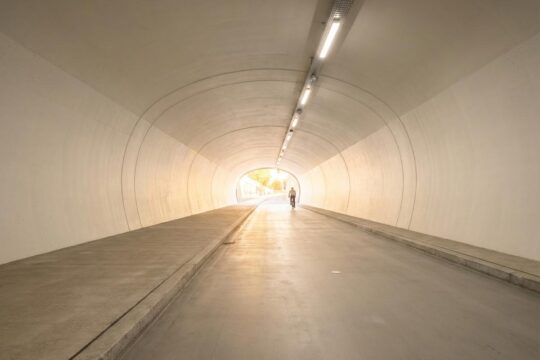 Der helle Velotunnel St. Gallen von innen zeigt die klare Trennung von Velo- und Fussweg. Tageslicht fällt vom Ausgang, eine Person im Hintergrund.
